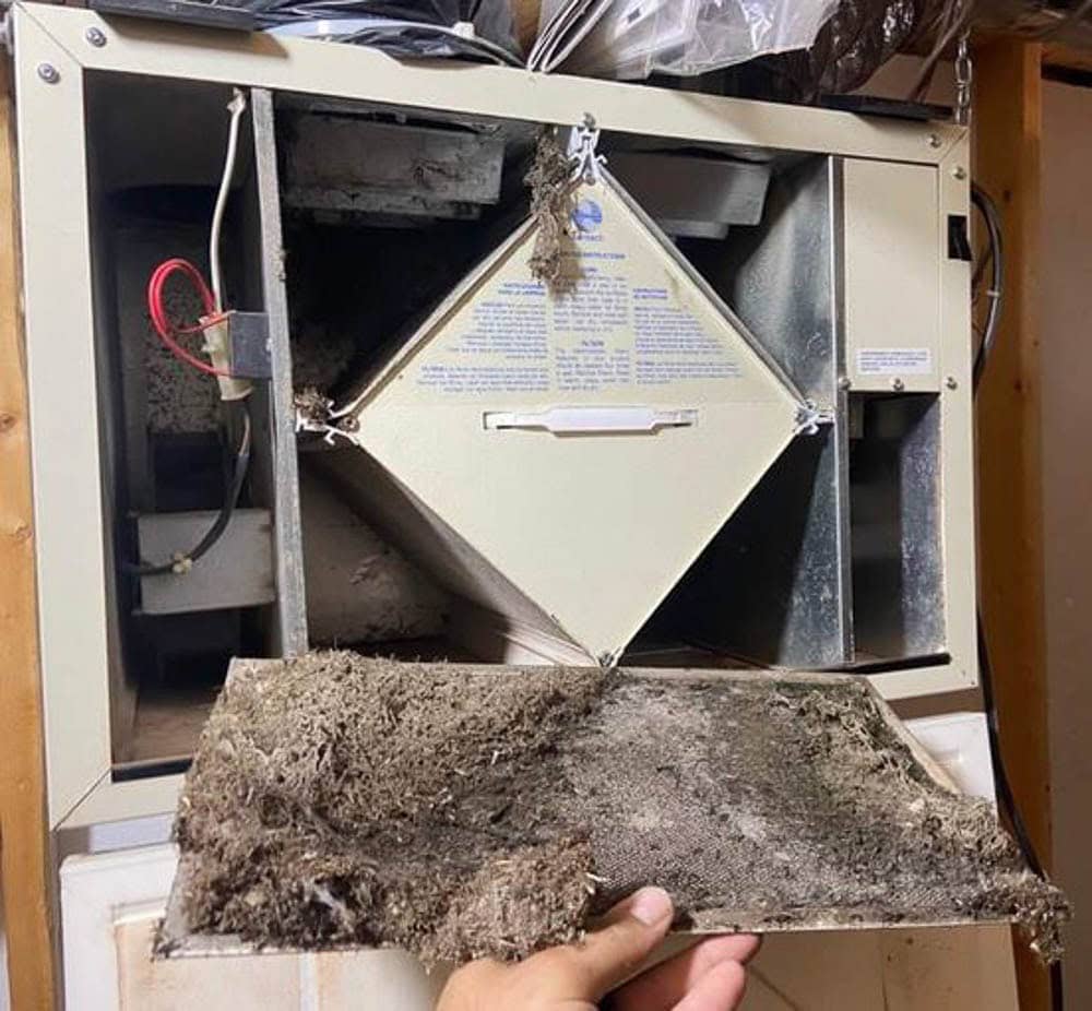Close-up view of a heavily clogged HVAC filter and heat exchanger with significant dust and debris buildup, impacting air quality and efficiency.