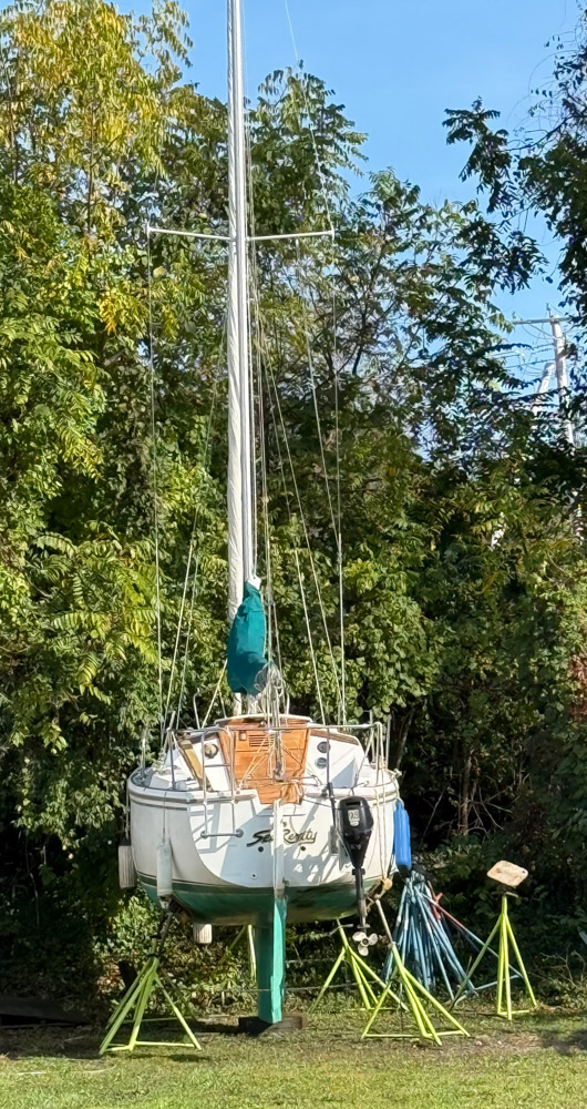 Sailboat on jack stands in wooded yard during fall, prepared for winter storage in the Hudson Valley.
