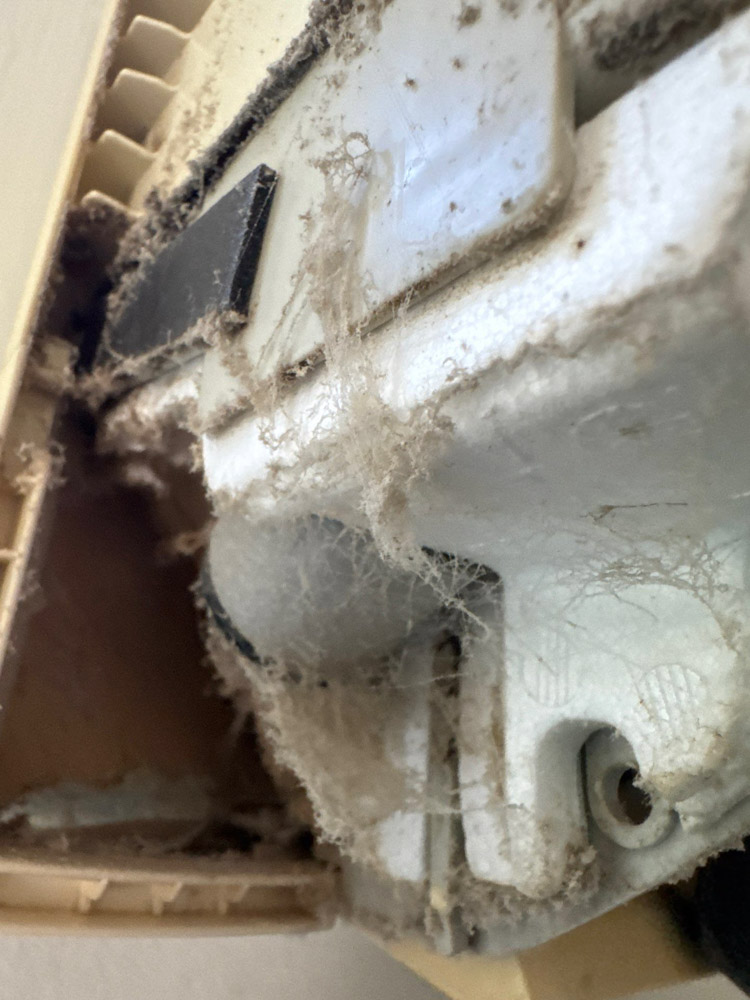 Extreme close-up of a mini split exterior caked with thick layers of dust, cobwebs, and debris, showing a heavily neglected and contaminated HVAC unit