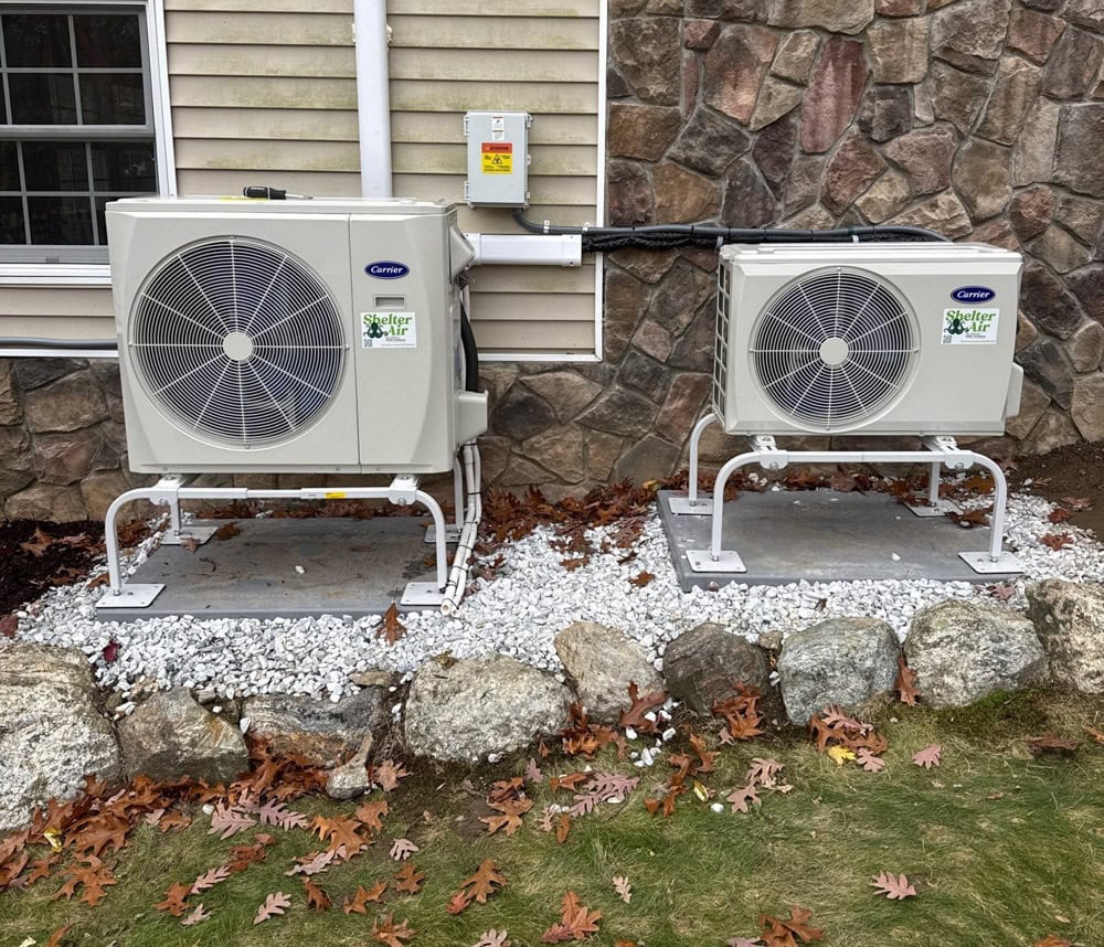 Outdoor heat pump condenser units installed on elevated stands against a home exterior, showing proper drainage and winter-ready setup for cleaner, energy-efficient heating in New Paltz, NY.