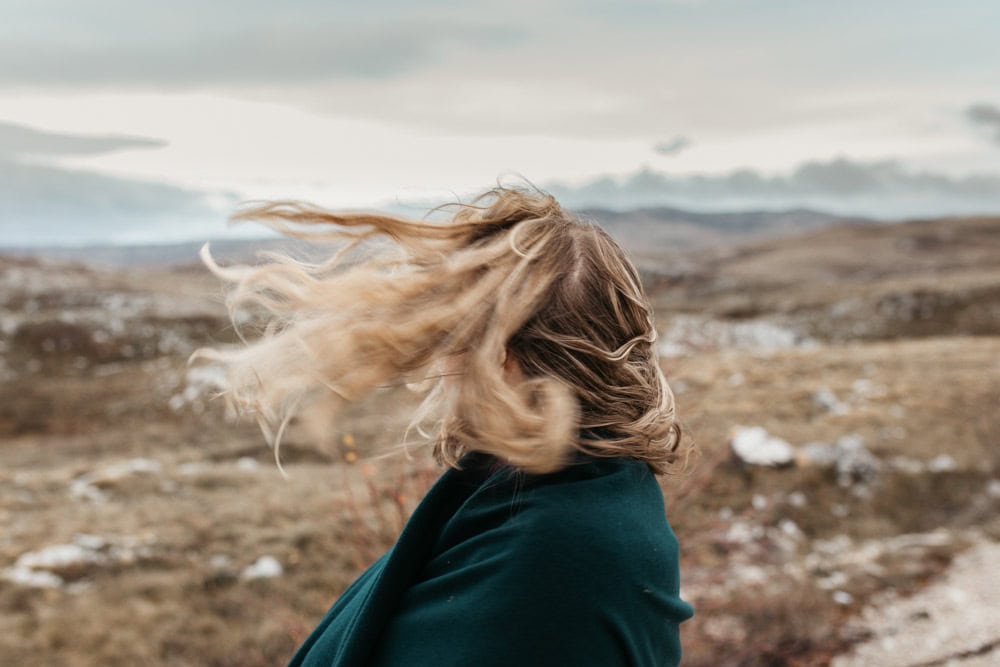 Woman standing outdoors with hair blowing strongly in the wind, illustrating the power of wind during a storm.
