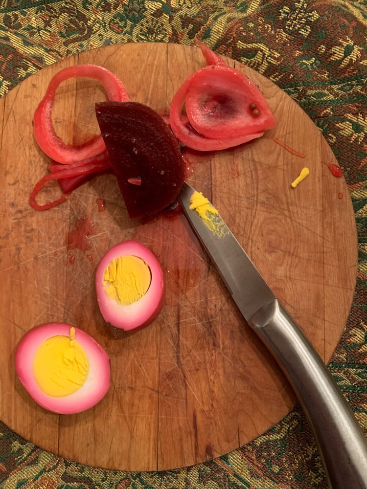 Homemade pickled beet eggs with sliced onions on cutting board in Croton-on-Hudson NY showing deep magenta egg whites and yellow yolks.